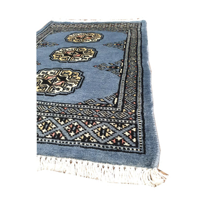 Angled fringe and border detail of Afghan Bokhara wool rug showing blue-grey pile, ivory gul motifs and dark edging