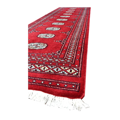 Angled view of Bokhara wool runner showing repeating ivory guls, layered red borders and white fringe