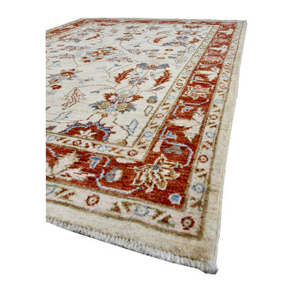 Angled view of beige Afghan Chobi wool rug showing its floral pile, rust-red border and finished edge