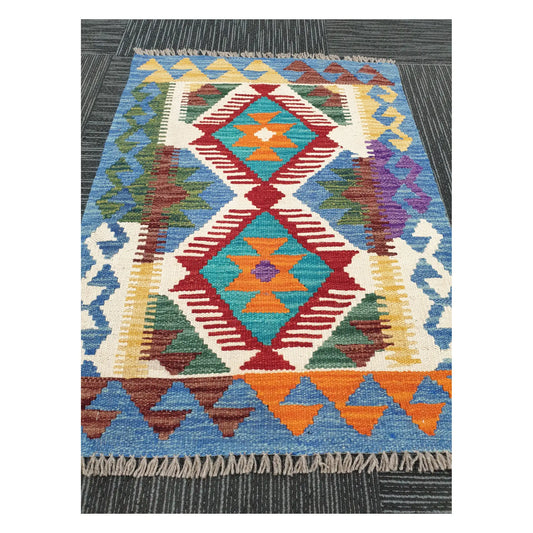 Angled view of Afghan Chobi Kilim wool flatweave rug showing blue geometric double medallion pattern and fringe, 84 x 60 cm