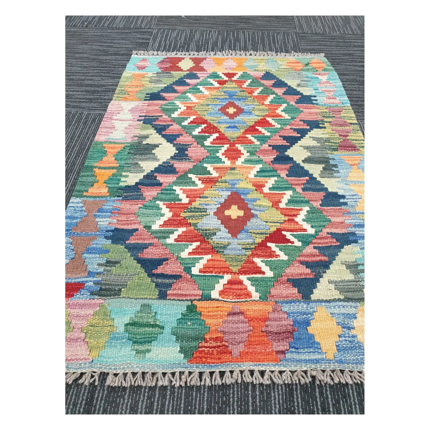 Angled view of Afghan Chobi Kilim flatweave rug showing geometric pastel double diamond pattern, 90 x 64 cm