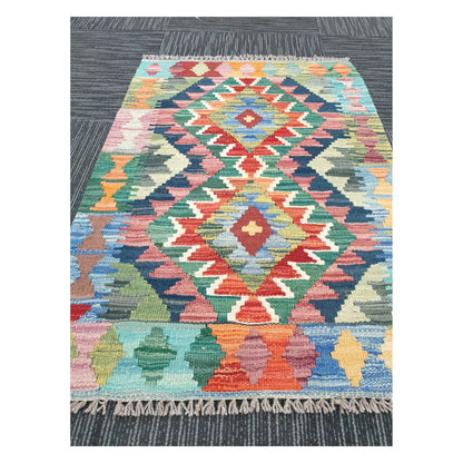 Angled view of Afghan Chobi Kilim flatweave rug showing geometric pastel double diamond pattern, 90 x 64 cm
