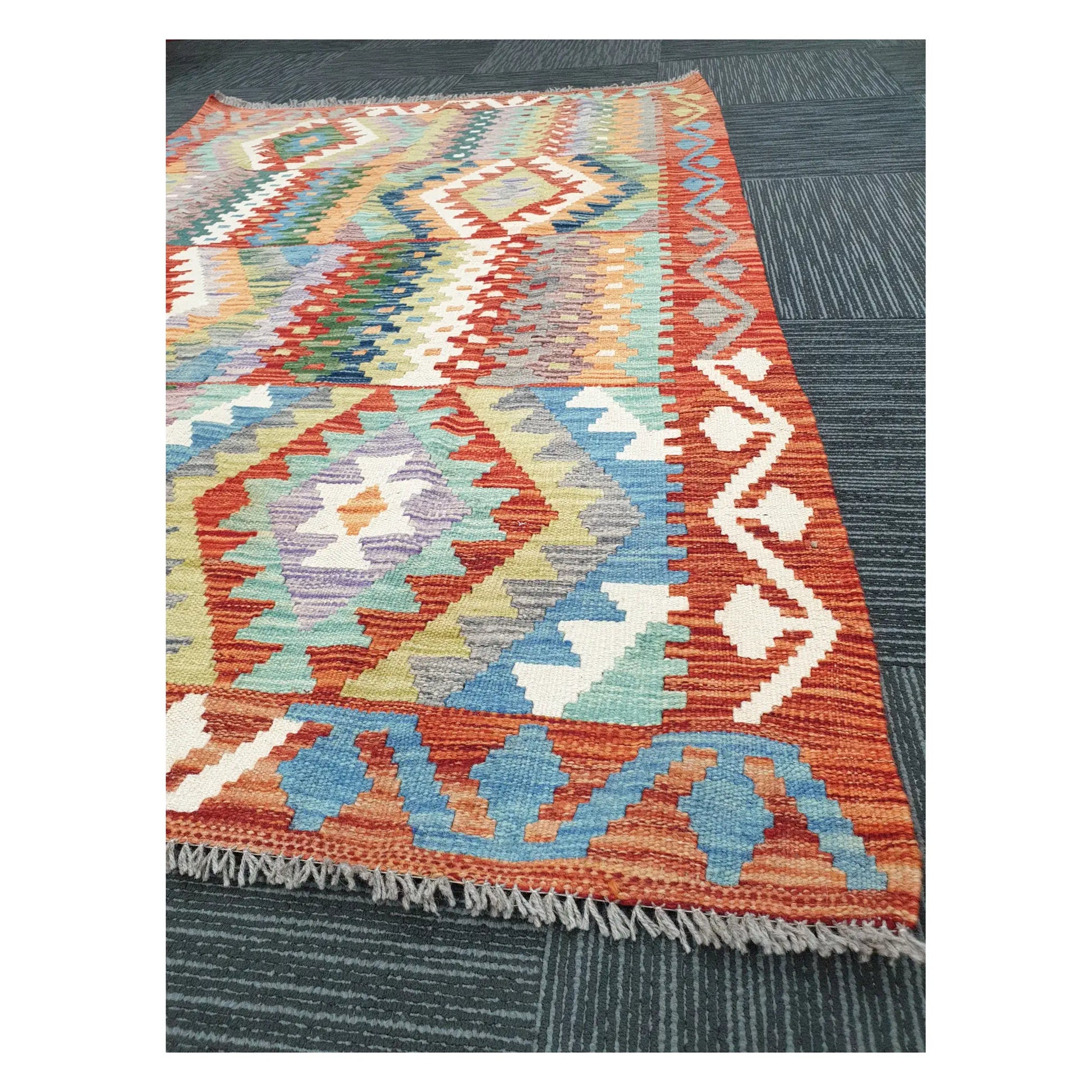 Angled view of Afghan Chobi Kilim rug showing terracotta border, fringe, and geometric flatweave detail, 180 x 122 cm