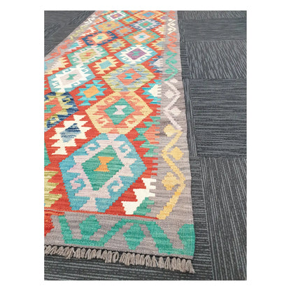 Angled view of Afghan Chobi Kilim runner showing pastel geometric diamond pattern and fringe, 291 x 81 cm