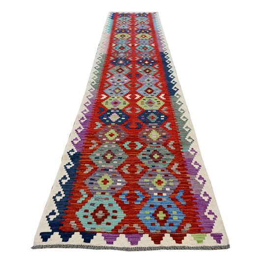 Full view of Afghan Chobi Kilim wool runner with paired multicoloured medallion chains on a coral-red field, 386 x 79 cm