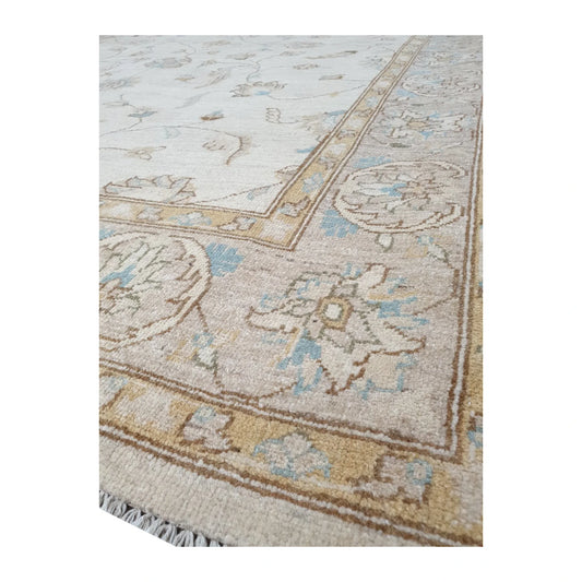 Angled corner detail of Afghan Chobi rug showing the warm tan floral border, pale blue accents and ivory fringe