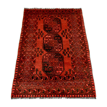 Angled full view of Afghan Ersari hand-knotted wool rug showing red field, dark motifs and geometric border, 155 x 105 cm