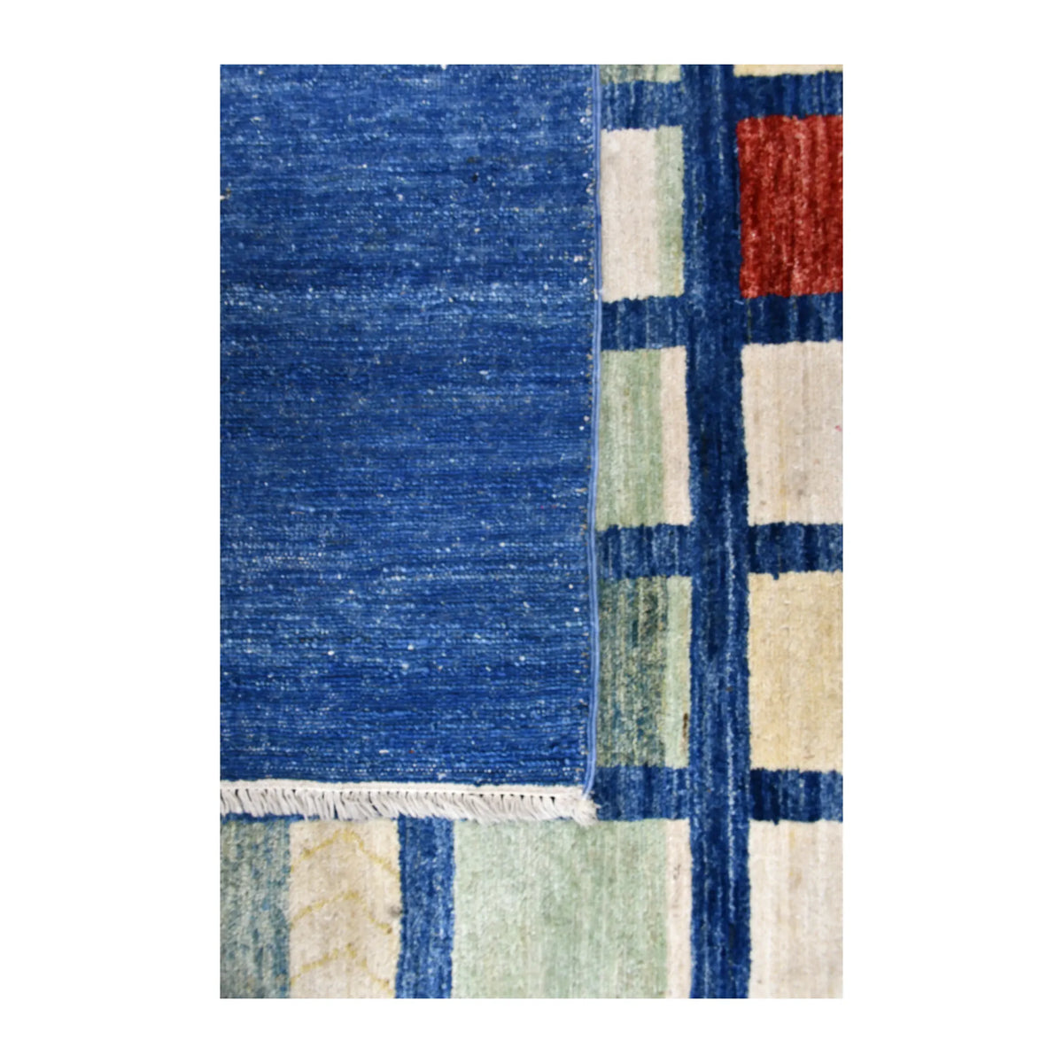 Close-up of the Afghan Gabbeh rug showing the reverse on its folded side beside the blue field and ivory-and-sage grid.