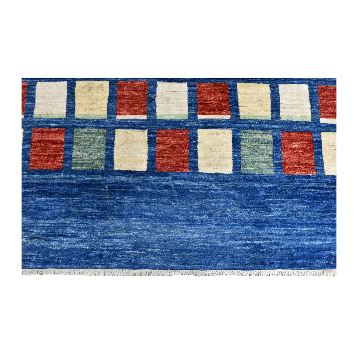 Fringed end of the blue Gabbeh rug beneath rows of ivory, rust and sage blocks