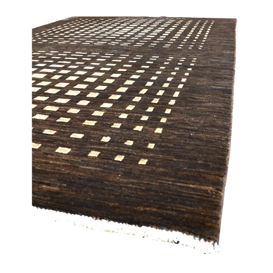 Angled view of Afghan Gabbeh wool rug showing its dark brown pile, repeated ivory motifs and pale fringe