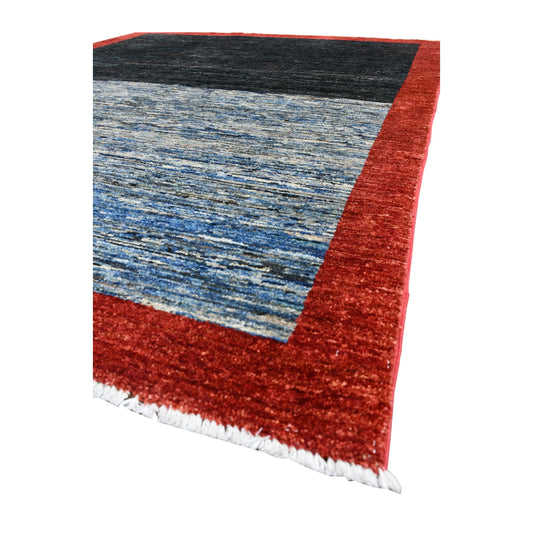 Angled view of Afghan Gabbeh wool rug showing its red border, dark navy and blue colour-block field and pale fringe