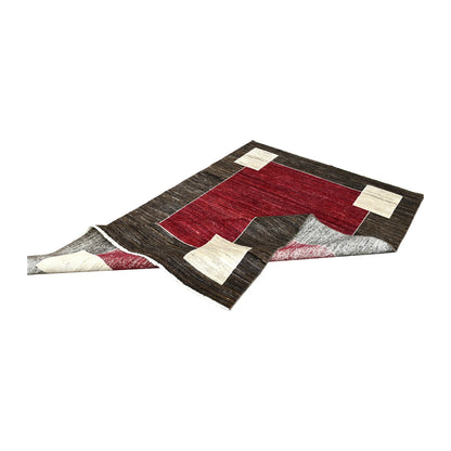 Folded view of Afghan Gabbeh hand-knotted wool rug showing its red field, brown frame, off-white blocks and fringe