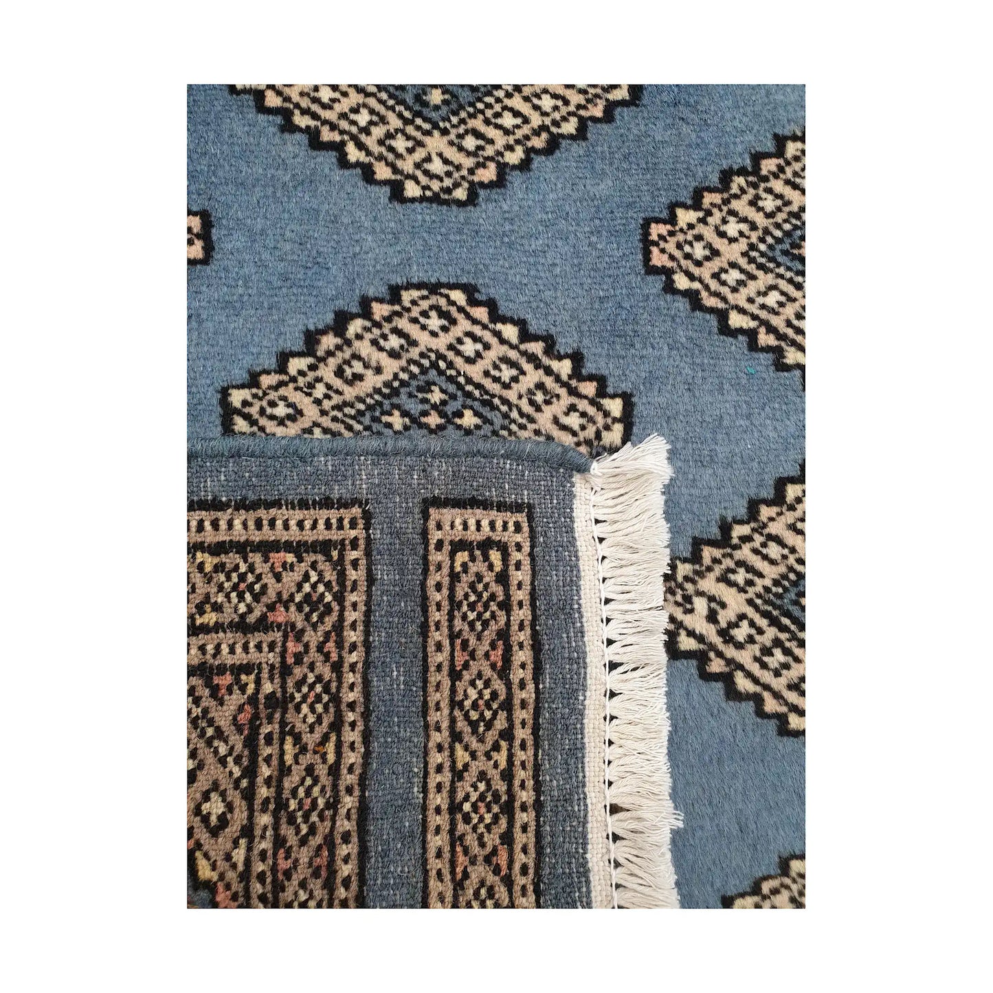 Folded corner detail of Afghan Jaldar wool rug showing the back of the rug, fringe and blue front pattern