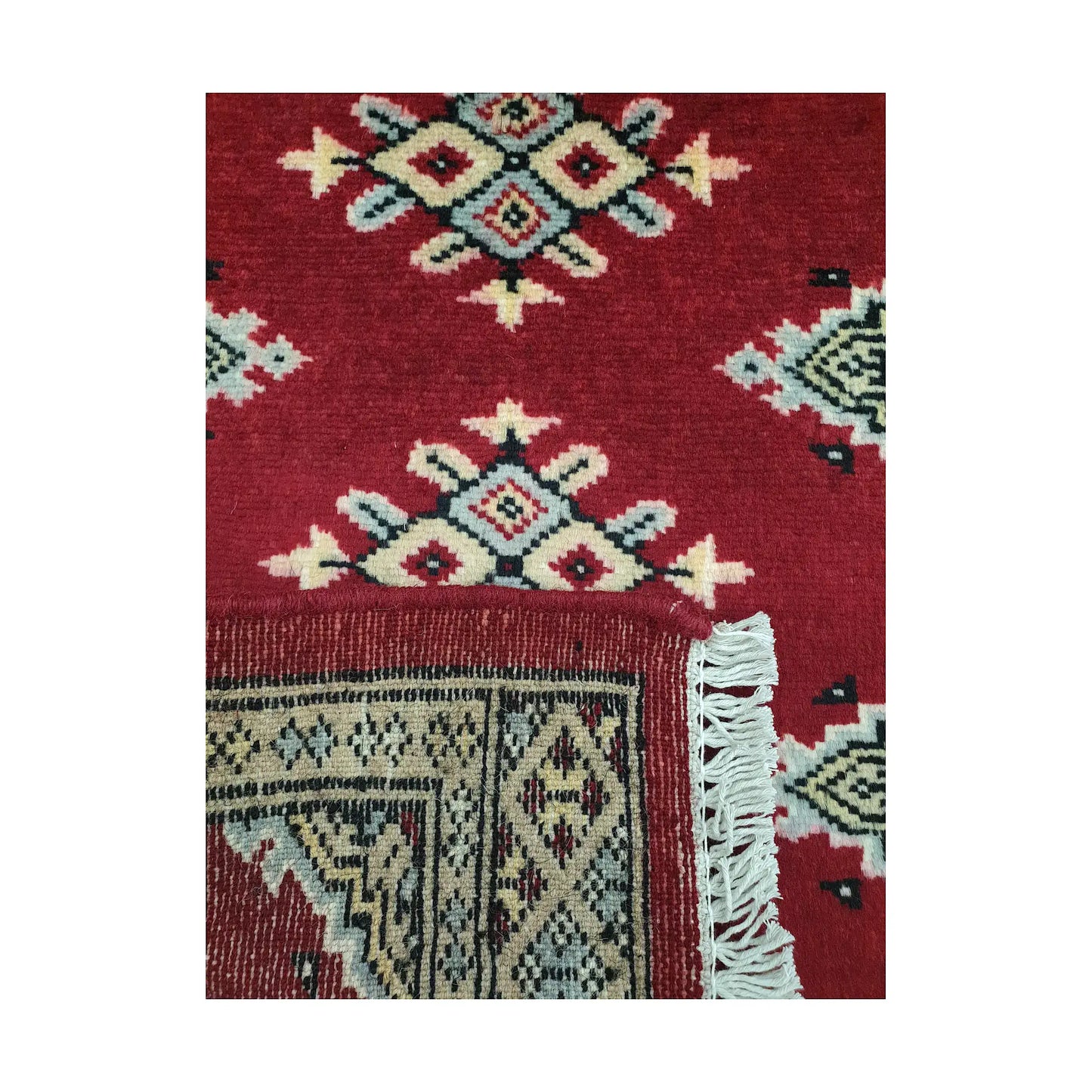 Folded corner detail of Afghan Jaldar wool rug showing the back of the rug, fringe and red front pattern