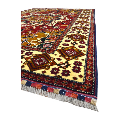 Angled view of Afghan Karghai rug showing its red field, patterned ivory diamond border and pale fringe