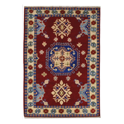 Full view of Afghan Kazak hand-knotted wool rug with red field, central blue medallion and cream border, 156 x 104 cm