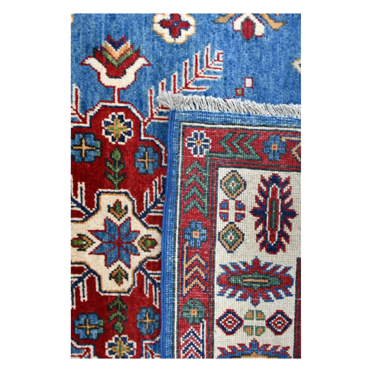 Folded-corner detail of Afghan Kazak rug showing the reverse weave, blue patterned front and pale fringe