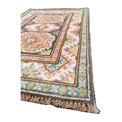 Angled corner and fringe view of Afghan Kazak wool rug showing cream field, muted red geometric motifs and light fringe