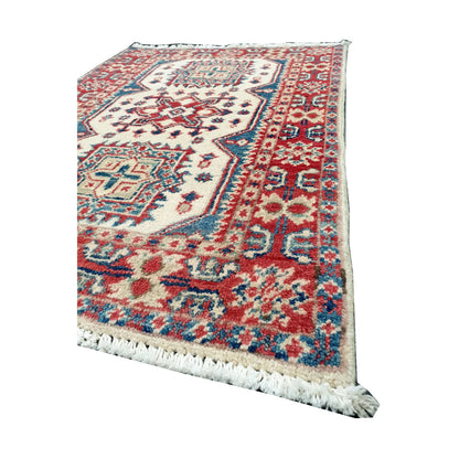 Angled corner and fringe view of Afghan Kazak wool rug showing cream field, muted red border detail, teal accents and light fringe