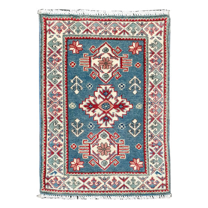 Full view of Afghan Kazak hand-knotted wool rug with blue field, central geometric medallion and cream patterned border, 90 x 61 cm