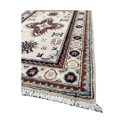 Angled corner and fringe view of Afghan Kazak wool rug showing ivory field, muted border detail and light fringe