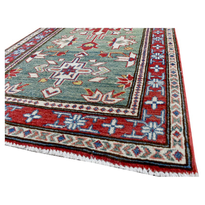 Angled corner and fringe view of Afghan Kazak runner showing the sage-green field, red border and wool pile