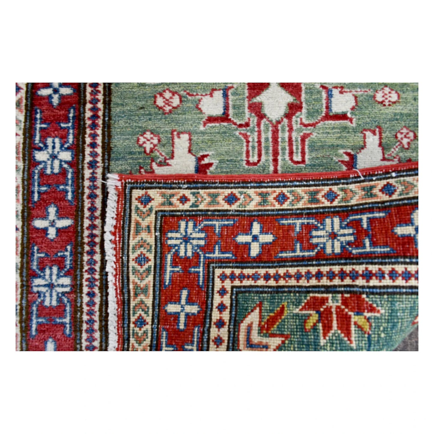 Folded corner of Afghan Kazak runner showing the front wool pile, reverse weave and geometric border construction