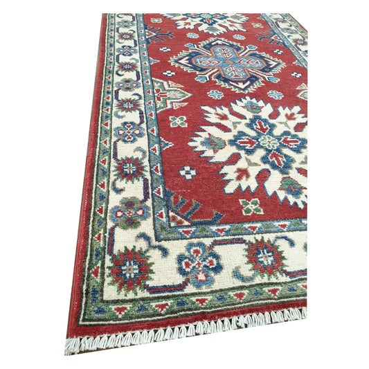 Close-up of Afghan Kazak wool runner rug corner showing light green border, red field and hand-knotted texture