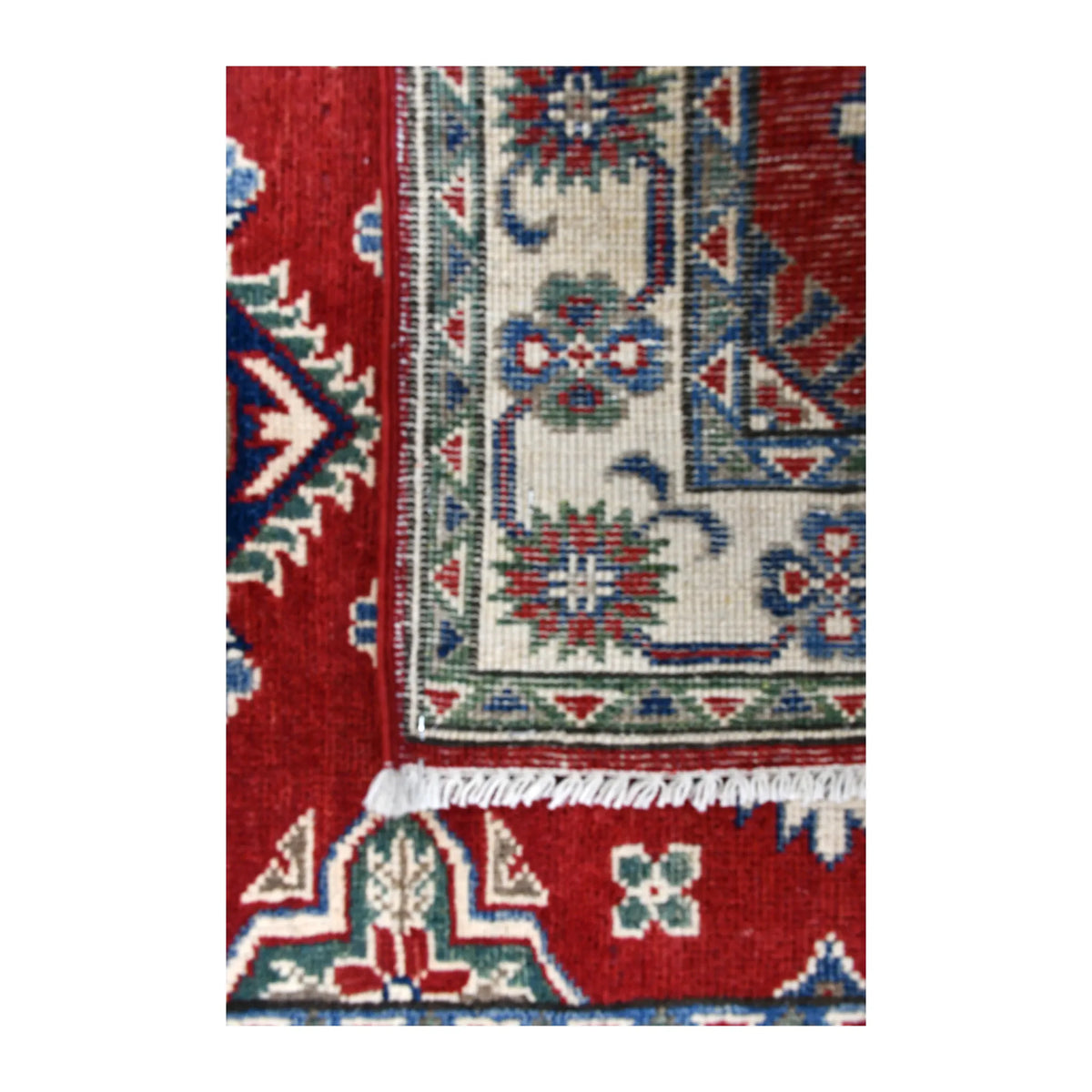 Folded-corner detail of Afghan Kazak runner showing the reverse weave beside its red patterned front, ivory border and white fringe