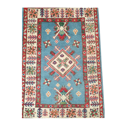 Close-up of Afghan Kazak wool rug showing the central diamond medallion, blue field and layered red and ivory border