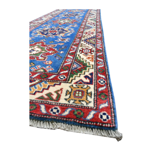 Angled view of Afghan Kazak runner showing its blue medallion field, patterned ivory border and pale fringe