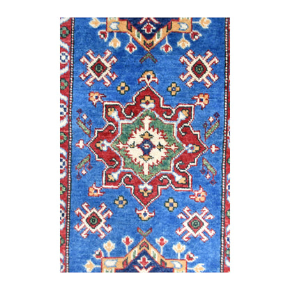 Close-up of a red stepped medallion with an ivory centre and smaller motifs on the Kazak runner’s blue field