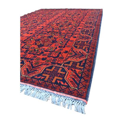 Angled view of Afghan Khal Mohammadi wool rug showing its red medallion field, dark navy border and pale fringe