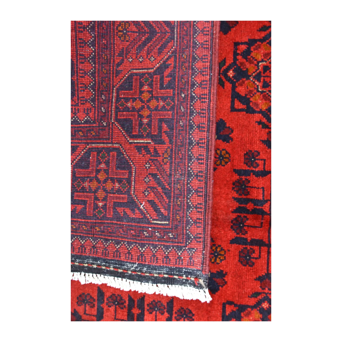 Folded-corner detail of Khal Mohammadi rug showing the reverse weave, red and dark navy front pattern and pale fringe