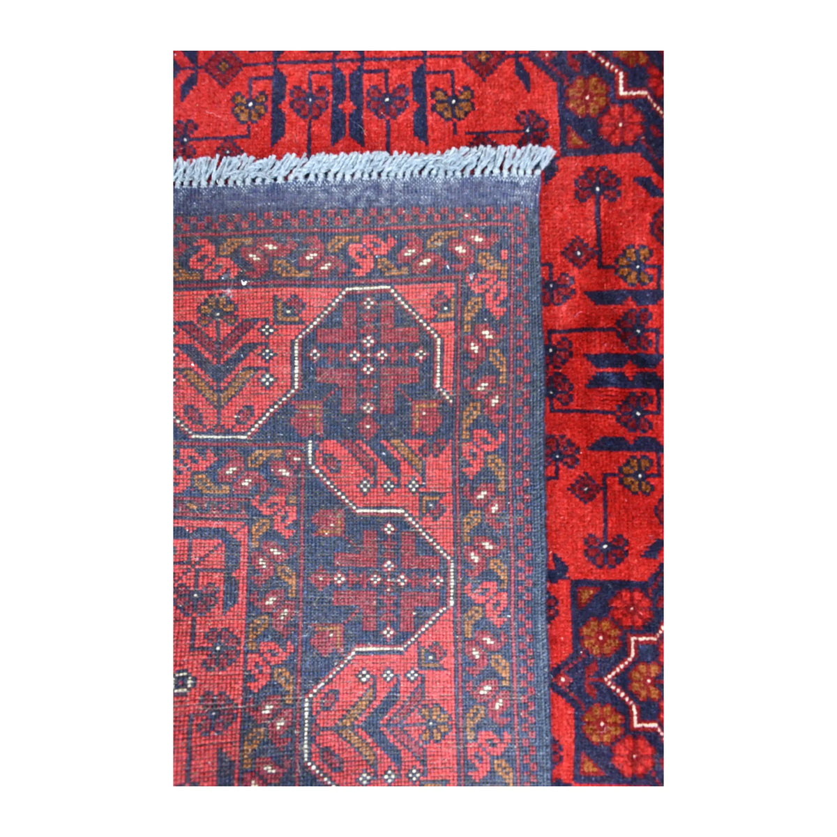 Folded-corner detail of Khal Mohammadi rug showing the reverse weave, red and dark navy front pattern and pale fringe