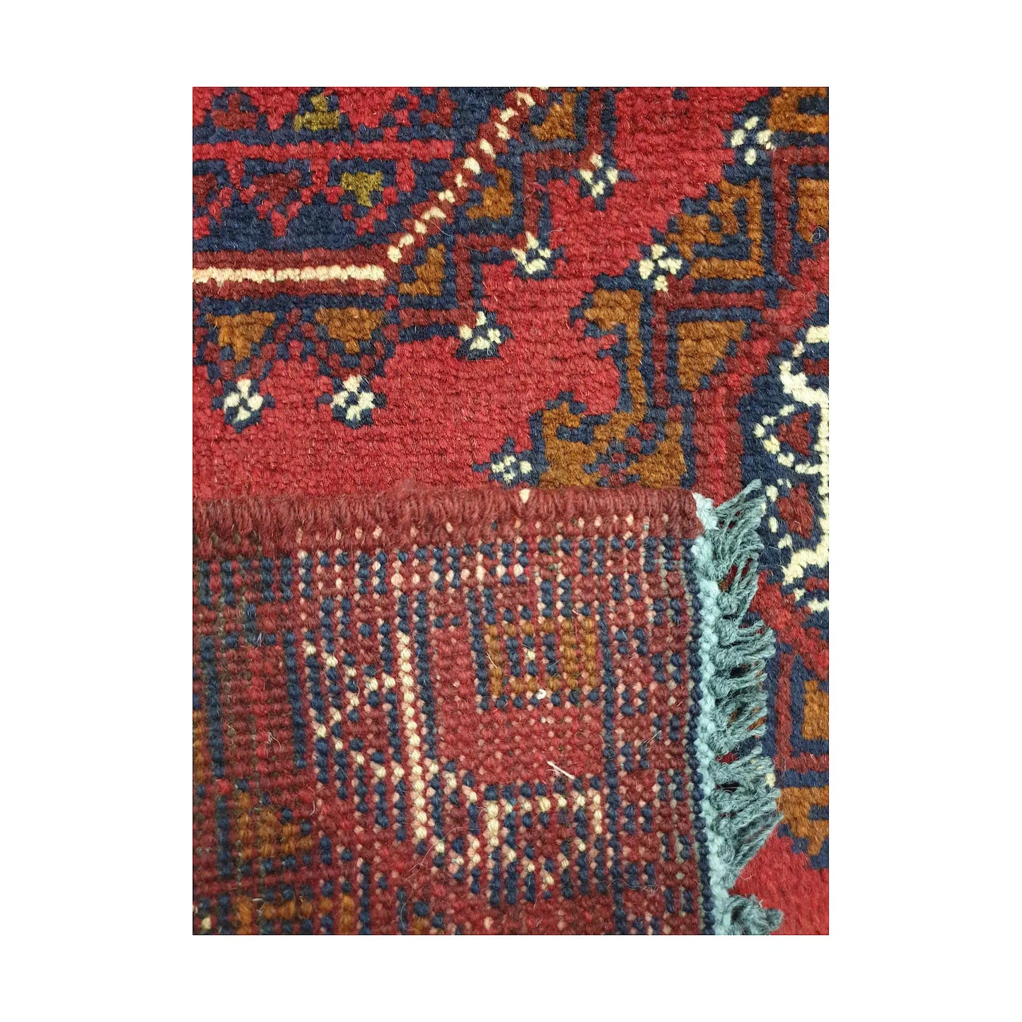 Folded corner detail of Afghan Khal Mohammadi wool rug showing the back, fringe and red front pattern