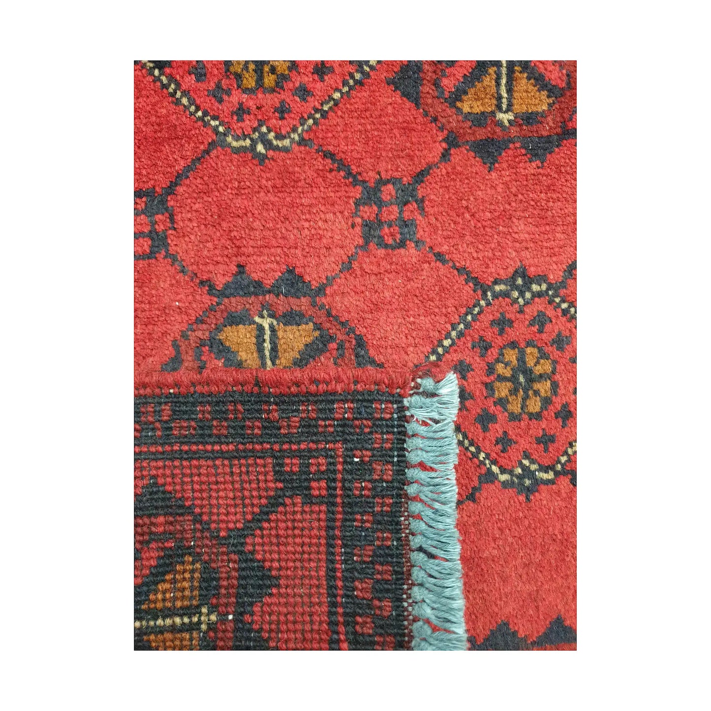 Folded corner detail of Afghan Khal Mohammadi wool rug showing the back, fringe and red patterned surface