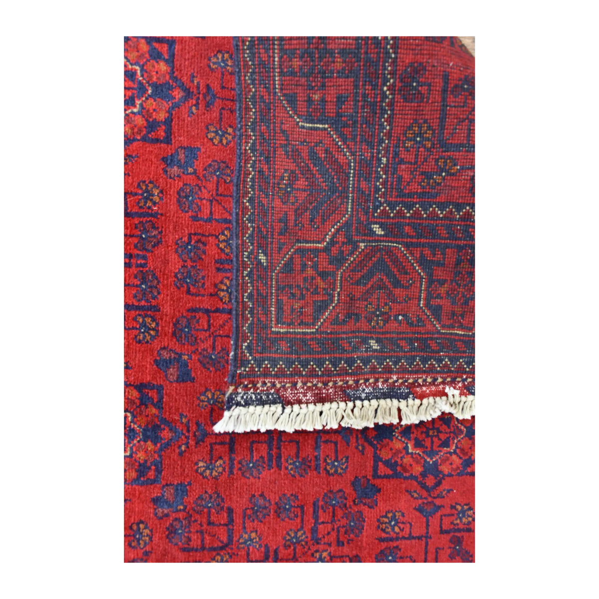 Folded-corner detail of Afghan Khal Mohammadi rug showing the patterned reverse beside its red floral front and ivory fringe