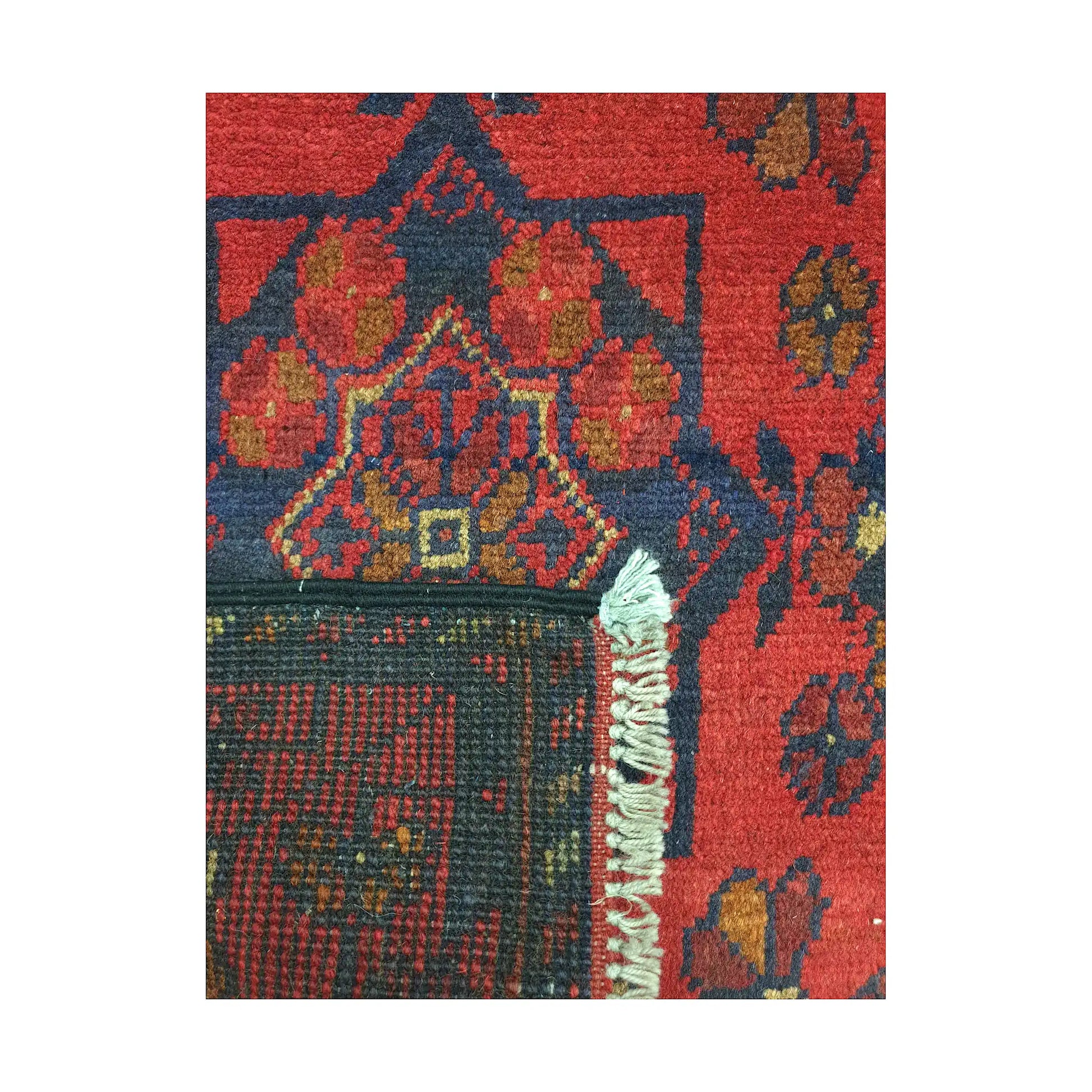 Folded corner detail of Afghan Khal Mohammadi wool rug showing the back, fringe and red front pattern