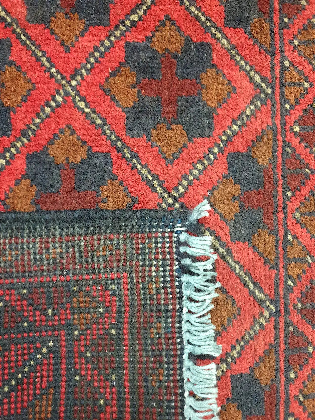 Folded corner detail of Afghan Khal Mohammadi wool rug showing the back, fringe and red front pattern