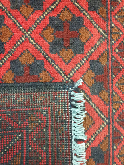 Folded corner detail of Afghan Khal Mohammadi wool rug showing the back, fringe and red front pattern