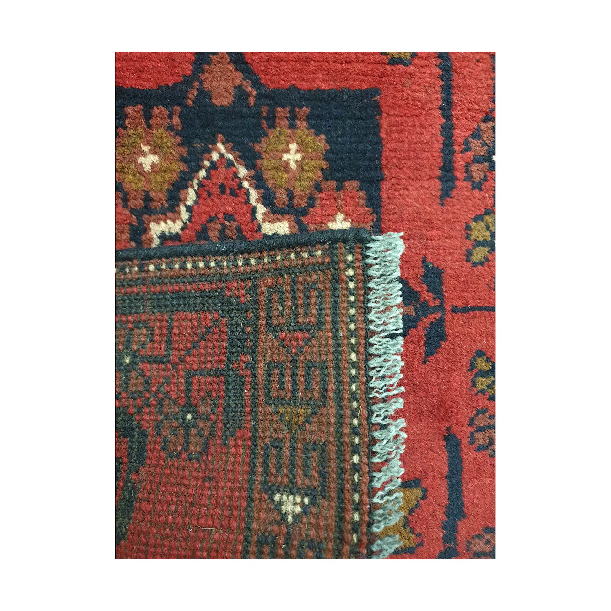 Folded corner detail of Afghan Khal Mohammadi wool rug showing the back, fringe and red front pattern