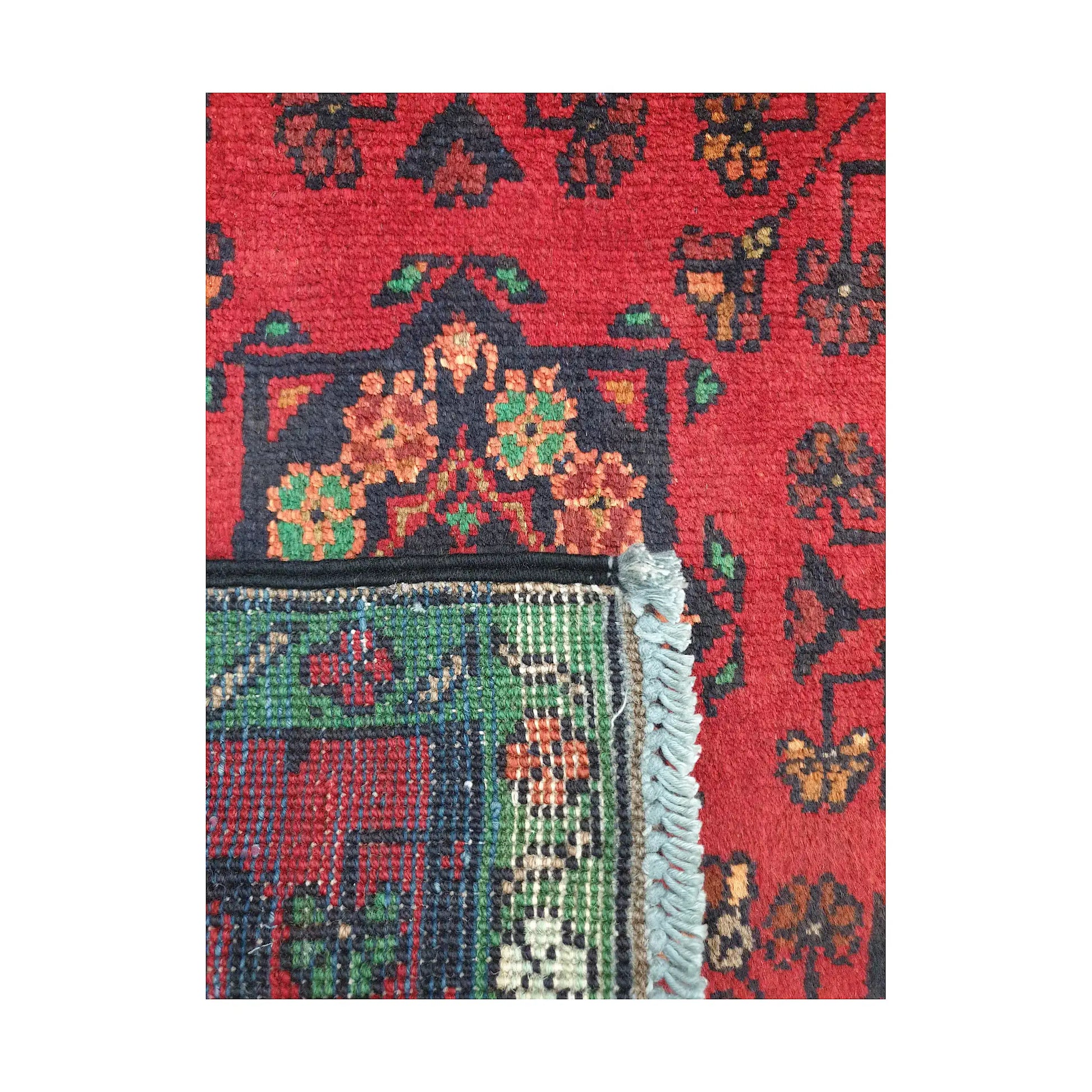 Folded corner detail of Afghan Khal Mohammadi wool rug showing the back, fringe and red-green front pattern