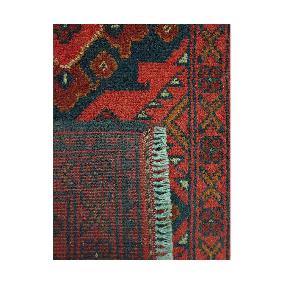 Folded corner detail of Afghan Khal Mohammadi wool rug showing the back, fringe and red geometric surface