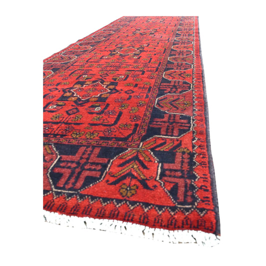 Angled view of Afghan Khal Mohammadi runner showing its dense red medallion field, broad geometric border and white fringe