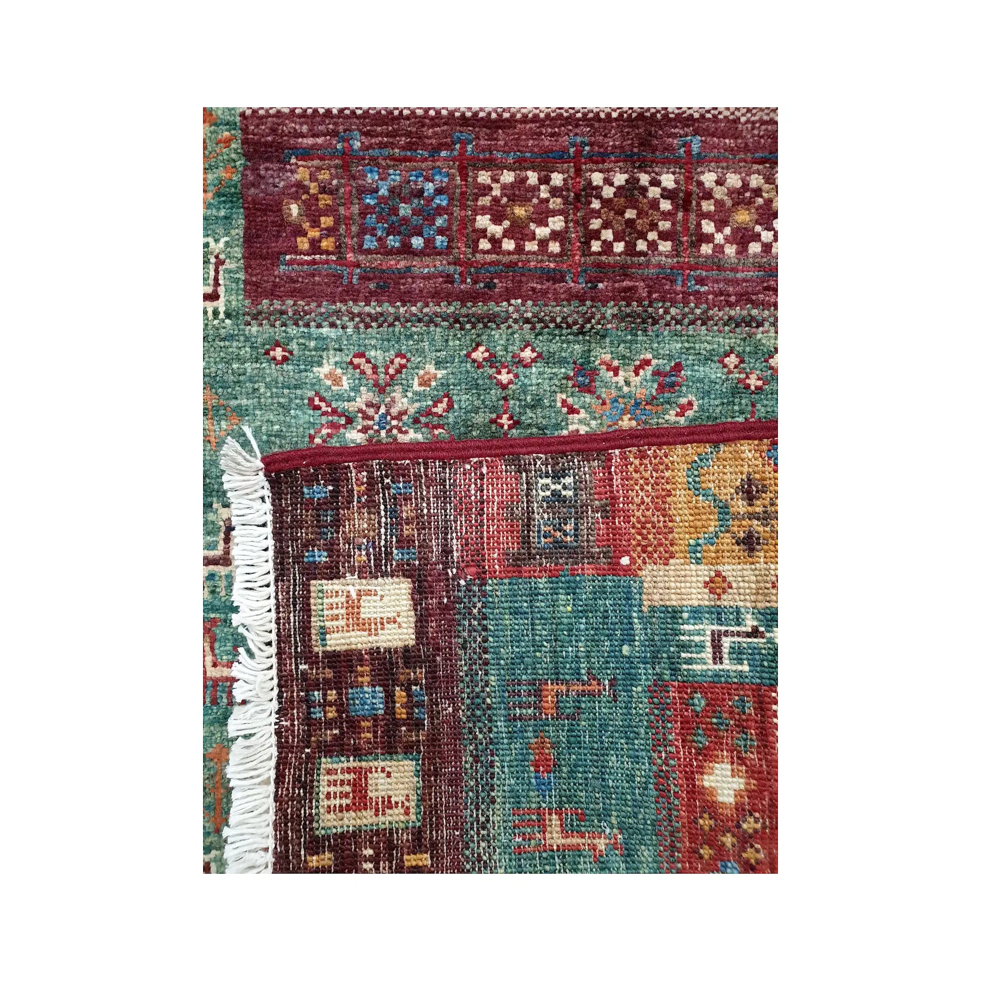 Folded corner detail of Afghan Khurjeen rug showing the back of the rug, fringe and front panel pattern