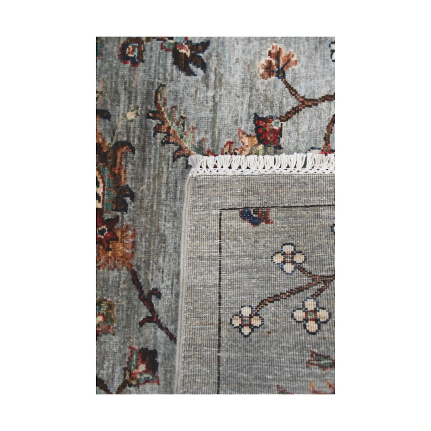 Folded corner detail of Afghan Khurjeen runner rug showing the back of the rug, fringe and grey floral front pattern