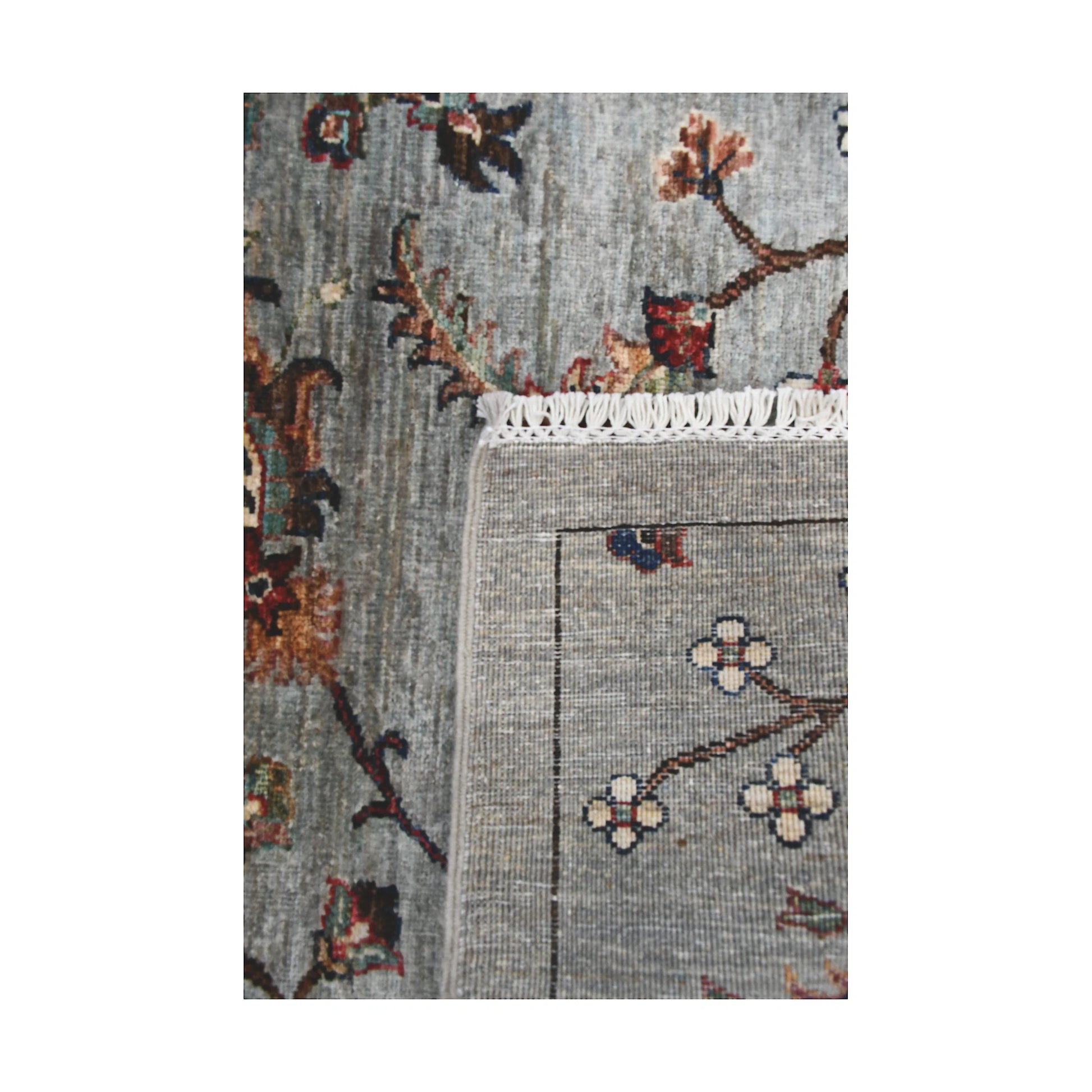 Folded corner detail of Afghan Khurjeen runner rug showing the back of the rug, fringe and grey floral front pattern