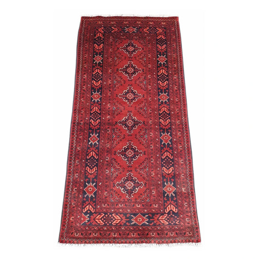 Full view of Afghan Kunduz hand-knotted wool runner rug with red field, repeating geometric medallions and layered navy borders, 192 x 89 cm
