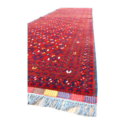Angled view of Afghan Kunduz runner showing its dense red geometric field, narrow patterned borders and blue-grey fringe